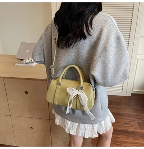 Detail of light green Boston bag with lace bow and pearl pendant worn on shoulder