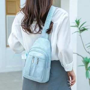 Close-up of light blue crossbody chest bag with double zippers and geometric strap