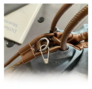 Detail of silver metal hook and brown leather handle on blue denim crossbody bag