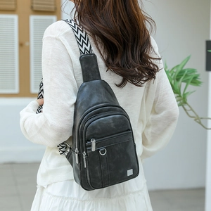 Detail of black vintage PU leather chest bag with woven strap and silver metal zippers