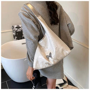 Detail der weißen Hobo-Tasche mit silberner Schmetterlingsschnalle und Metallic-Besatz