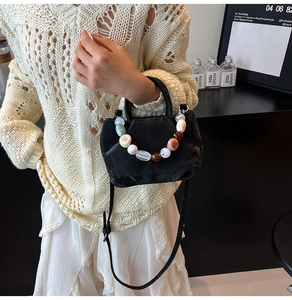 Détail d'un sac seau noir avec une poignée en perles colorées et bandoulière