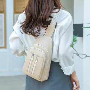 Detail of beige crossbody chest bag featuring woven geometric strap and dual zip pockets