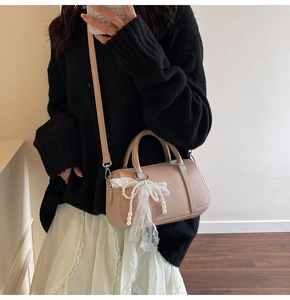 Detail of beige lychee grain leather boston bag with lace pearl bow charm and shoulder strap