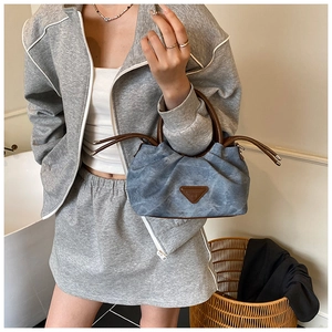Detail of blue denim pleated handbag featuring brown leather handle and triangle patch