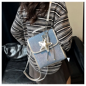 Detail of light blue denim crossbody bag with silver star pendant and metallic fringe