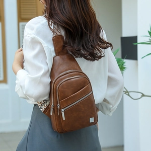 Detail of vintage brown leather chest bag showing three zipper pockets and woven strap