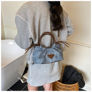 Detail view of blue pleated canvas handbag with leather handles and triangle logo patch
