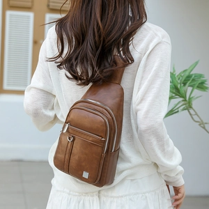 Outdoor shot of brown vintage PU leather chest bag showing textured finish and metal logo