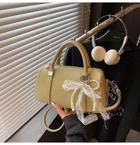 Detail of green textured leather Boston bag with pearl lace bow charm and shoulder strap