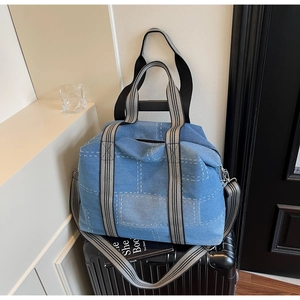 Close-up of blue denim tote bag with white stitching detail on a travel suitcase