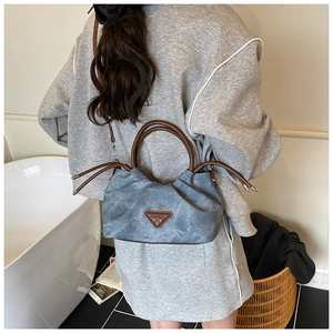 Detail of blue denim pleated bag with brown leather handles and iconic triangle patch