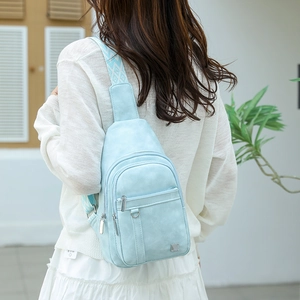 Light blue crossbody chest bag with wide woven strap shown in an outdoor setting