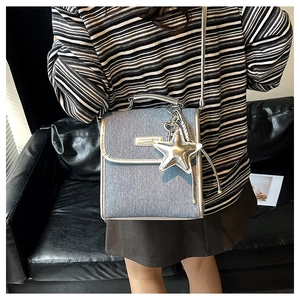 Detail of light blue denim crossbody bag with silver star charm and metallic hardware
