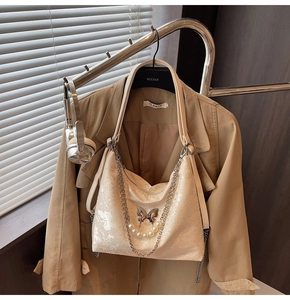 Détail du sac beige avec pendentif papillon argenté et perles sur une surface texturée