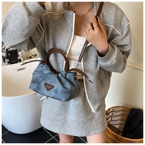 Detail of blue denim pleated bag featuring brown leather handle and triangle emblem
