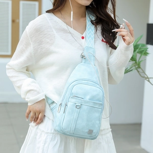 Light blue faux leather sling bag with patterned wide strap worn by model in sunlight