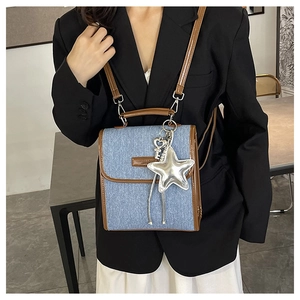 Detail of denim shoulder bag with brown leather trim and silver star pendant accessory