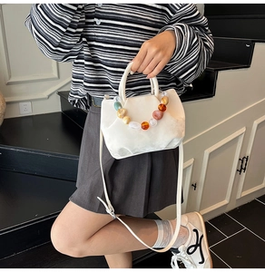Vue détaillée du sac seau en cuir blanc avec poignée en perles colorées et plis