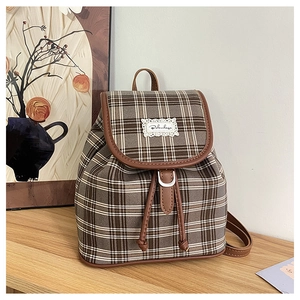 Close-up of vintage brown plaid backpack with leather trim and magnetic closure
