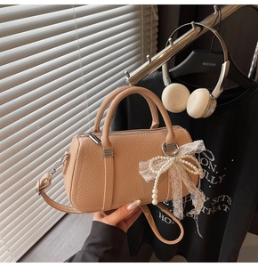 Close-up of beige lychee textured leather pillow bag with pearl bow bag charm