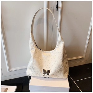 Nahaufnahme der cremefarbenen Hobo-Tasche mit Schmetterlings-Metallanhänger und Prägung