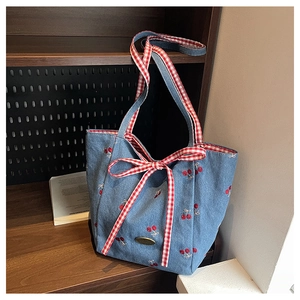 Close-up of light blue canvas tote bag with red cherry embroidery and a large gingham bow
