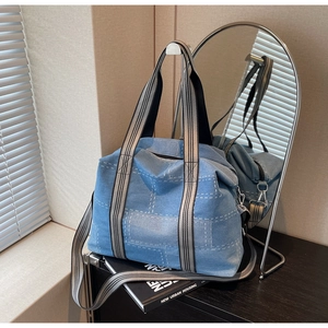 Detailed close-up of large denim tote bag featuring white stitching and striped strap