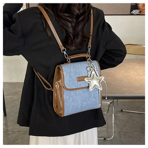 Detail of light blue denim backpack with brown leather trim and silver star charm