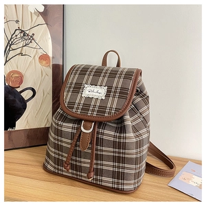 Detail of a brown plaid canvas backpack with leather trim and drawstring closure on a table
