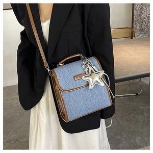 Detail of blue denim shoulder bag with brown leather trim and silver star pendant