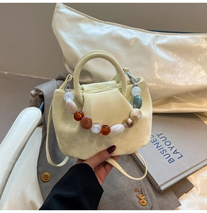 Détail du sac seau plissé beige clair avec une chaîne décorative en perles marbrées