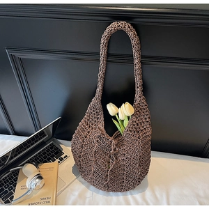 Detail of hollow knit tote bag in brown with floral accents on minimal bedding