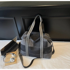 Detail of large denim tote bag with patchwork design and striped handles on white fabric