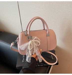 Detail of pink faux leather bowling bag with lace bow and pearl charm on leather sofa
