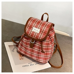 Detail view of red plaid canvas backpack with brown leather trim and metal buckle