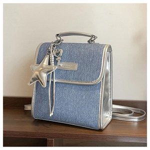 Close-up of denim shoulder bag with silver star and heart charms on wood surface
