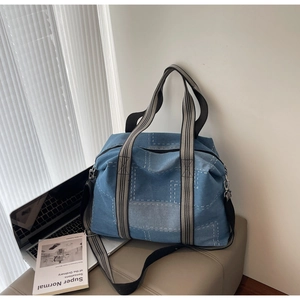 Detail of blue denim tote bag with white patch stitching and striped webbing handles