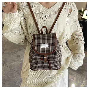Detail of plaid canvas backpack with leather trim and drawstring closure on model