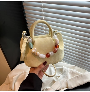 Détail d'un sac beige avec chaîne en perles marbrées et texture plissée élégante