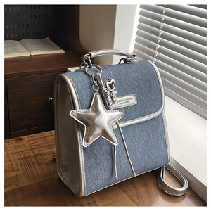 Close-up of denim handbag with silver star pendant and metallic leather trim on wooden table