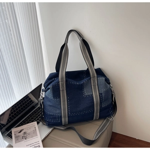 Detail of blue denim tote bag with contrast stitching and striped woven handles