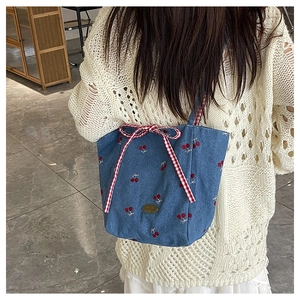 Detail of blue denim tote bag featuring red cherry embroidery and a checkered bow tie