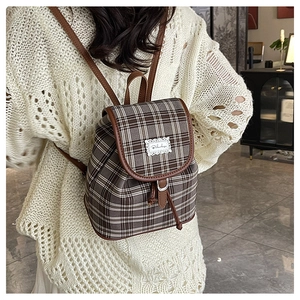 Detail of a brown plaid canvas backpack with leather straps on a model's back