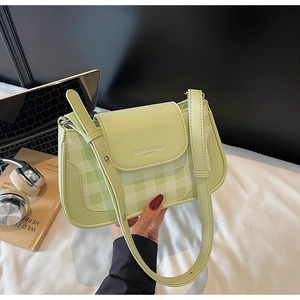 Close-up of green plaid shoulder bag with metal logo detail and leather trim finish