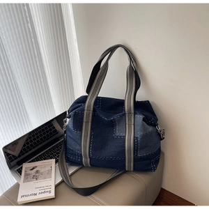Detail of patchwork denim tote bag with contrast stitching and striped web handles
