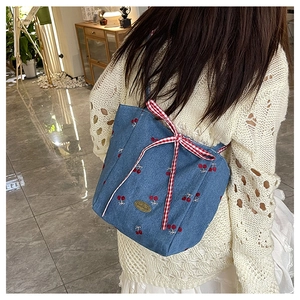 Detail of blue denim tote bag with red cherry embroidery and a red gingham bow accent