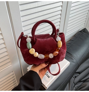 Détail du sac seau en daim bordeaux avec poignée en perles de résine colorées sur canapé