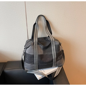 Detail of grey patchwork denim tote bag with thick white stitching on a black leather sofa