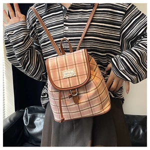 Detail of pink plaid canvas backpack with brown leather trim and metal clasp on model